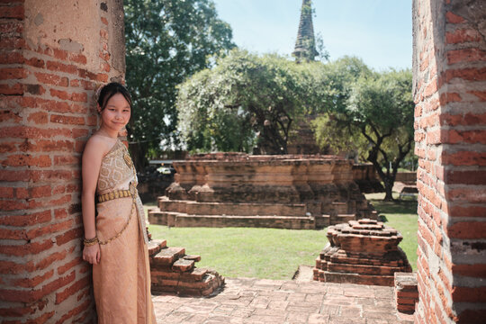 Portrait of Asian teenage girl dressed in Thai traditional outfit with cheerful smile and looking at camera, holiday travel in Ayutthaya, Southeast Asia, ancient ruins heritage,  tourist destination.