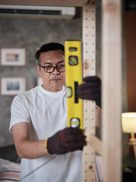 Asian mature man determines, installing furniture with carpentry tools, checking accuracy with spirit&nbsp;level, home improvement, craft making, hobby wooden workshop, expert handyman, active lifestyle.