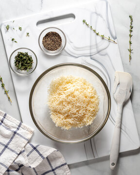 A mixing bowl filled of parmesan cheese with thyme and pepper above.