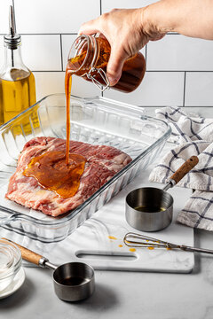 A hand pouring homemade marinade onto a flank steak.