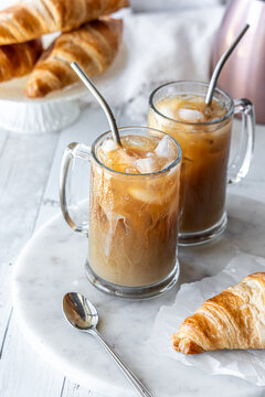 Servings of iced coffee served with croissants, against a light background.