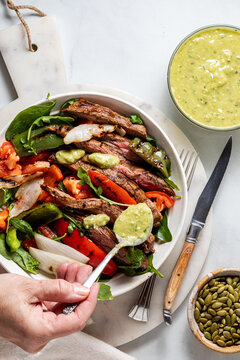A hand topping a fajita steak bowl with avocado cilantro dressing.