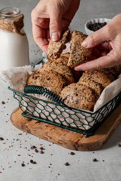 Hands breaking a quinoa cookie in half with a basket full of the cookies behind.