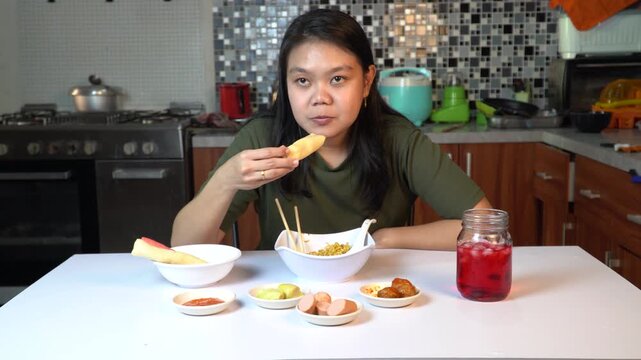 Young Asian woman eating spring roll and noodles at home kitchen table
