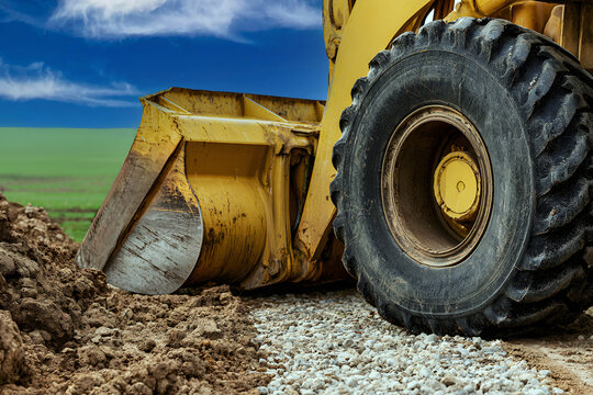 close-up of a heavy yellow wheel loader excavator bucket and large tire working on dirt soil at a construction site under a blue sky background.