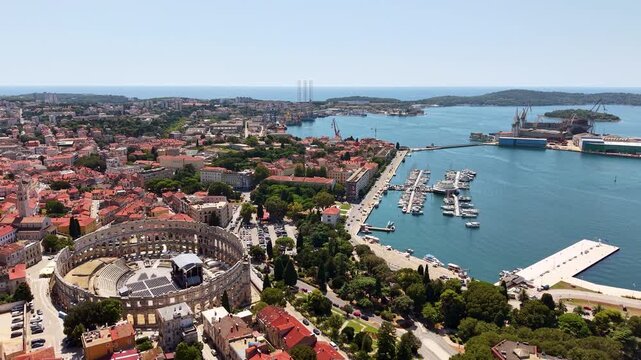 High-altitude aerial drone view of the Roman amphitheatre, the old town and the shipyard cranes along the harbour, Pula, Croatia