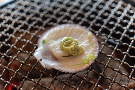 Fresh scallop its shell topped herb butter sliced green onion cooking over wire grill for savory seafood barbecue meal