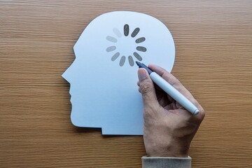 Obraz premium Hand drawing a loading icon onto a white paper human head silhouette. Mental fatigue, brain fog, cognitive delay, slow learning concept.