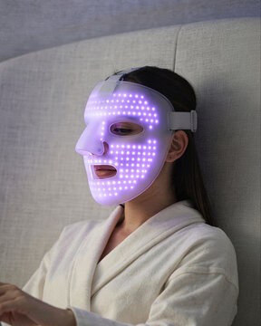 Woman Relaxing in LED Light Therapy Facial Mask at Home