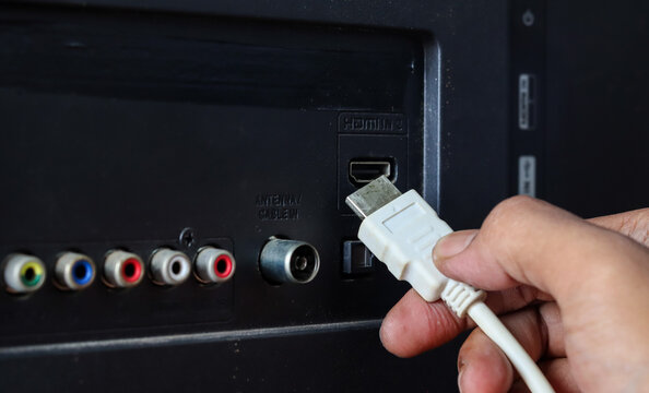 Close-up of a hand plugging a white HDMI cable into an HDMI port on the back of a television.
