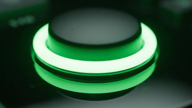 Human finger pressing a glowing green power button on a control panel
