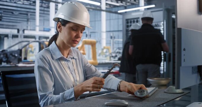 In Smart Factory, Female Engineer Uses Vernier Caliper to Inspect Metal Part at Desk. Male Colleagues Work at Large Server Cabinet Nearby to Ensure Smooth Automated Workflows. Concept of Industry 4.0.