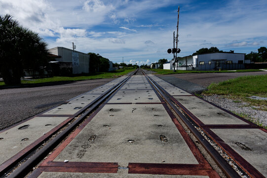 Low-angle photo of rusty train tracks stretching into the distance across gravel and wooden sleepers in a suburban St. Petersburg, FL green setting, suggesting travel, solitude, perspective, industria