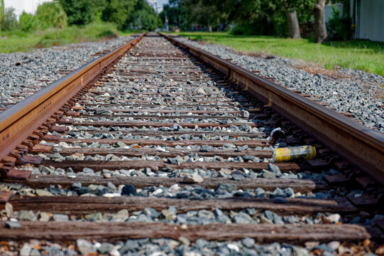 Low-angle photo of rusty train tracks stretching into the distance across gravel and wooden sleepers in a suburban St. Petersburg, FL green setting, suggesting travel, solitude, perspective, industria