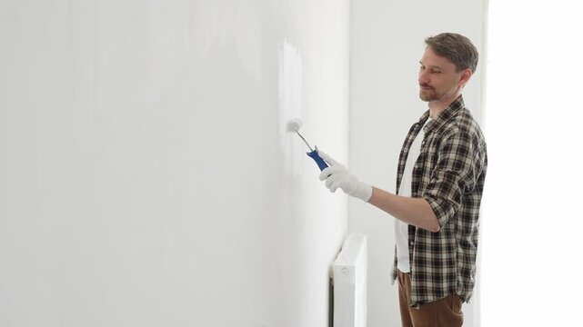 Professional house painter wearing gloves painting a white wall with a paint roller, working on a home renovation project, creating a fresh and clean look