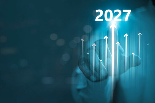 Year 2027 Business Growth Target Concept with Hand Pointing to Glowing Upward Arrows.
