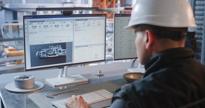 Inside Glass Office, an Engineer Works at Dual Screens Showing Car Parts While Automated Conveyor Robots Assemble Cars in Plant. Smart Robotics Optimize Industry 4.0 Workflow. AI Manufacturing.