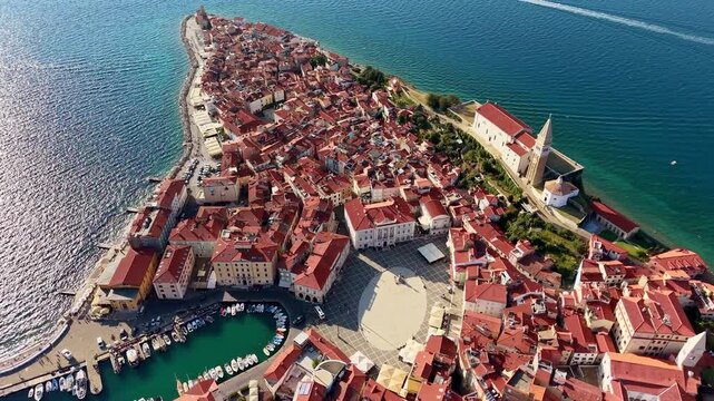 Aerial drone view of the oval main square, the harbour and the church above the red rooftops of the old town, Piran, Slovenia