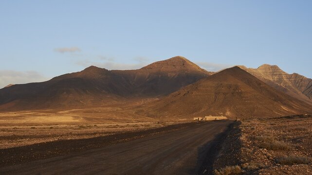 Morning light, Wild South, Jandia, barren landscape, non-asphalted road, reddish brown hills, blue sky, few clouds, Fuerteventura, Canary Islands, Spain