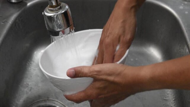 person washing bowl with sponge and dish soap in sink under running  water from faucet, human hands cleaning white bowl with soapy sponge and rinsing, kitchen hygiene, daily chores and domestic life