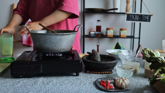 Home cook Adding granulated sugar with spoon simmering dish on portable burner