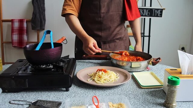 Chef ladling rich tomato Bolognese sauce over plate of cooked spaghetti noodles using wooden spoon