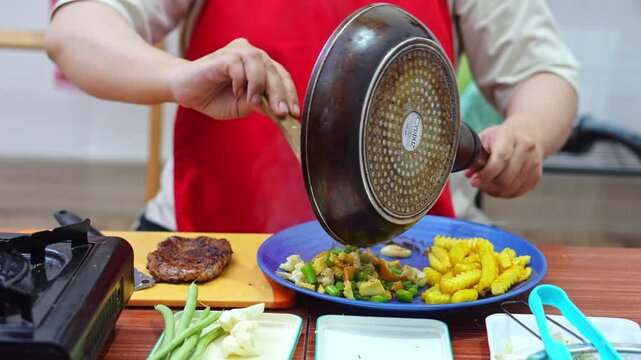Chef serving steaming saut&eacute;ed vegetables onto plate during steak dinner preparation