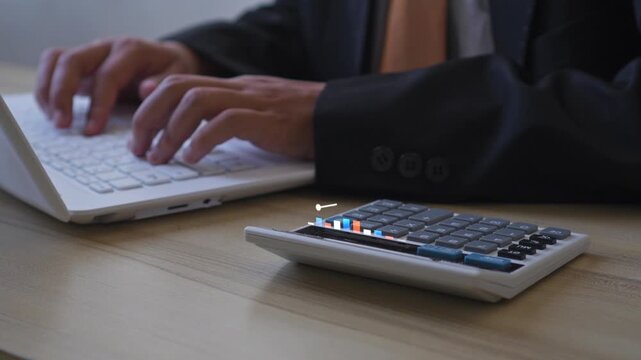 Businessman types on laptop while 3D animated financial chart grows above calculator on his desk
