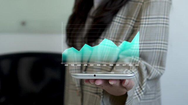 Businesswoman taps tablet while projecting animated holographic chart showing financial growth