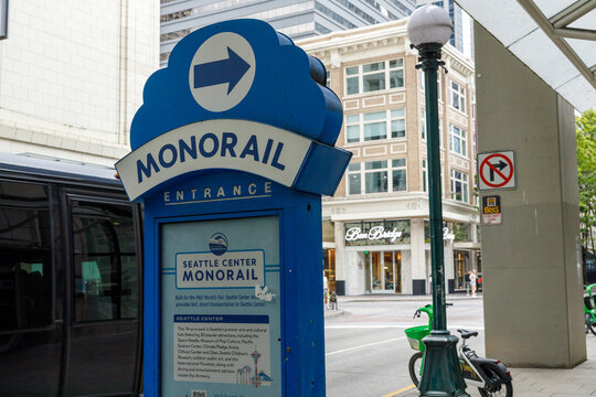 A blue Monorail Entrance sign for the Seattle Center Monorail stands on a downtown sidewalk, the Ben Bridge jewelers storefront and a rental bike visible behind.