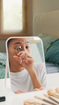 Vertical Screen : Young happy Asia girl beauty blogger look at mirror makeup use eyelash curler before mascara in bedroom. Lifestyle people, Make up Natural look, Skin Care Cosmetics, Morning routine.