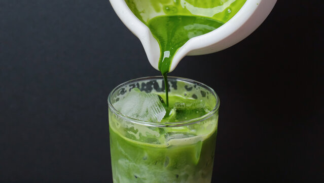 pouring rich green matcha tea over clear ice in glass.