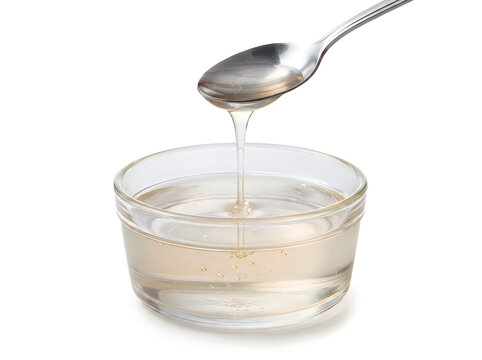 A clear, viscous liquid syrup pouring from a metal spoon into a small glass bowl, isolated on white background