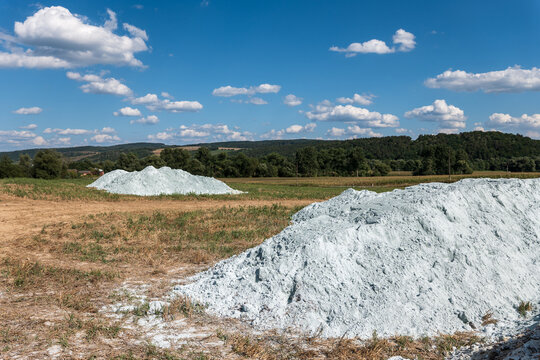 Piles of agricultural lime on a harvested stubble field before spreading, illustrating autumn soil liming, pH correction, soil amendment and preparation for the next crop.