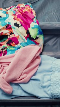 Vertical Screen : Top view. Young happy and exciting Asian female ready for summer holiday prepare suitcase throw cloth accessories stuff in bag in bedroom. Preparing luggage for summer vacation trip.