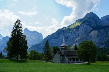 peaceful church in mountain landscape with stone pathway and wooden trees foreground perspective natural setting serene and dynamic composition for travel and architecture themes. © DIgnat_Switzerland