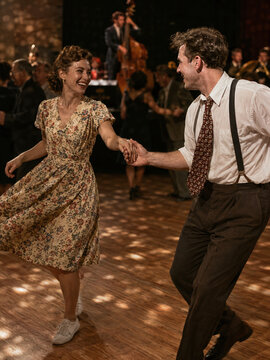 Joyful vintage couple dancing lindy hop swing dance to live music in a ballroom