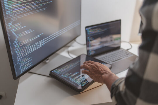 Software developer coding on laptop and tablet in a modern workspace. Close-up of programming workflow, software engineering, debugging source code, and multi-device application development.