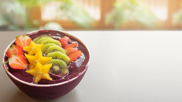 Colorful acai bowl with mango stars and kiwi with blurred tropical cafe background banner.