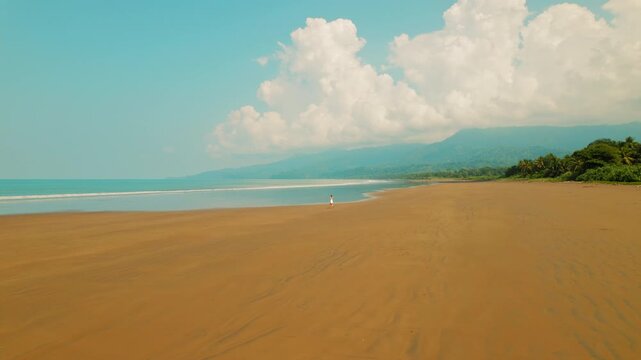 Lone traveler walks on expansive sandy beach under bright tropical sky