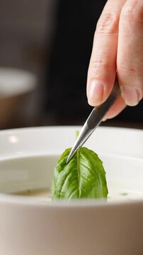 Hand places fresh basil leaf into creamy white soup
