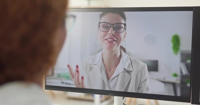 Businesswoman talks during a remote video conference. Monitor view shows a woman in glasses gesturing while explaining ideas to a colleague. Modern remote work communication concept today.