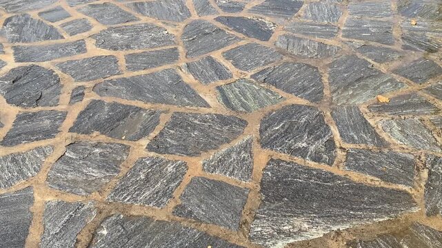 Rain falling on grey irregular flagstones set in light brown mortar.