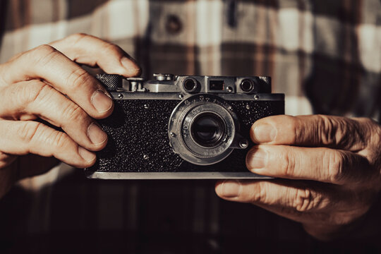 Closeup of hands holding vintage rangefinder film camera. Man holding antique classic analog camera detailed retro photography equipment hobby journalist and nostalgia concept backdrop