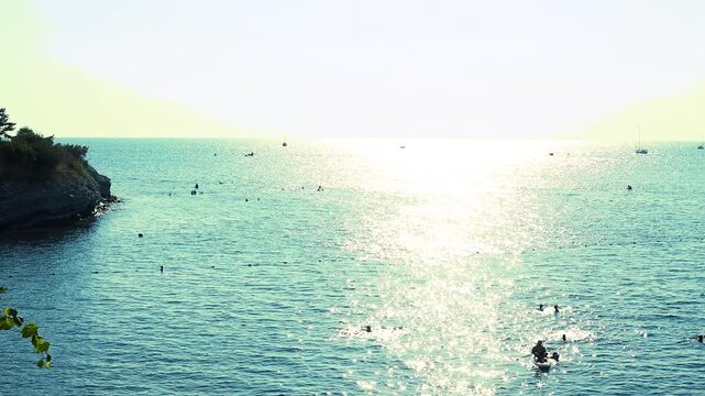 Two paddleboarders navigate calm waters, surrounded by distant hills and boats, highlighting a peaceful coastal scene under a clear sky