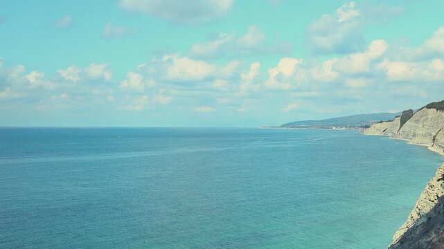 Small fishing boat glides through calm blue waters near a rocky coastline, with distant mountains and a clear sky enhancing the peaceful coastal landscape