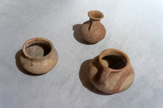 Ancient handmade clay pottery on light background. Three terracotta vessels: two pots and one small jug with painted stripes. Archaeological artifacts with natural texture and cracks.