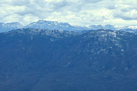 Vast mountain range covered in dense evergreen forest under a cloudy sky, Blackcomb Gondola. Whistler, BC, Canada