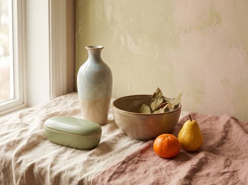 Still life with ceramic vases, fruits, and decorative bowl on table