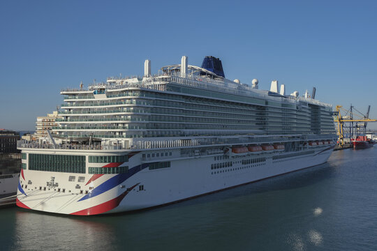 Massive gigantic modern cruiseship cruise ship liner Iona or Arvia in Cadiz, Spain during summer Mediterranean cruising with harbor and container port infrastructure